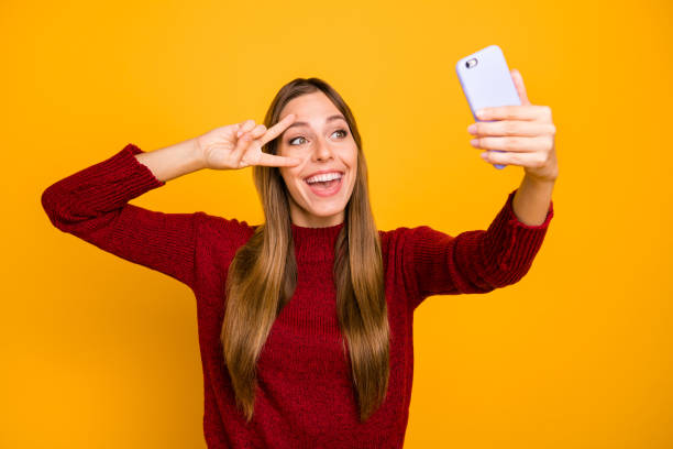 istock Pretty lady holding telephone hands making selfies showing v-sign wear knitted pullover isolated yellow background 1163895032