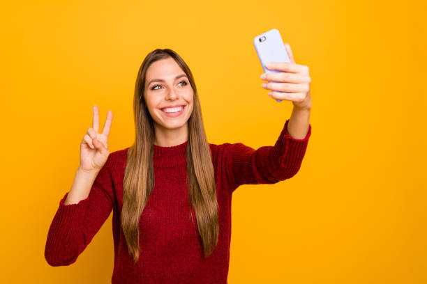 istock Pretty lady holding telephone hands making selfies showing v-sign wear knitted pullover isolated yellow background 1163895935
