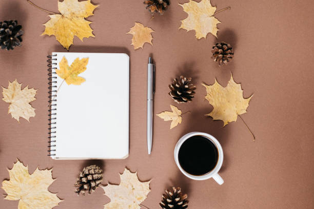 istock Workspace with golden maple leaves, coffee cup, bumps, notebook and pen on brown background. Creative composition. Autumn or Winter concept. Flat lay, top view 1163897018