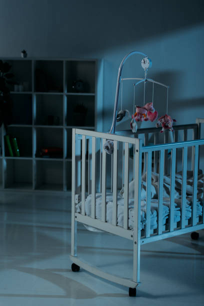 Crib with mobile and cupboard standing in dark room