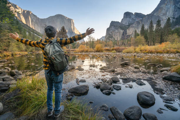 istock Young man arms open at Yosemite valley from the river, reflections on water surface 1163900973
