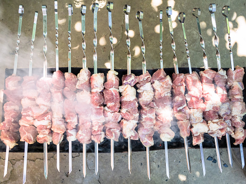 many raw skewered shish kebabs (shashlyk) from pork meat are cooked on outdoor brazier with hot coal