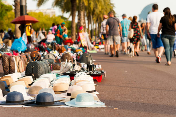 imigrantes africanos vendedores ambulantes chamados "manteros" vendem produtos falsificados ao longo do passeio ao pôr do sol com turistas andando no porto de barcelona - port de barcelona catalonia spain barcelona city - fotografias e filmes do acervo