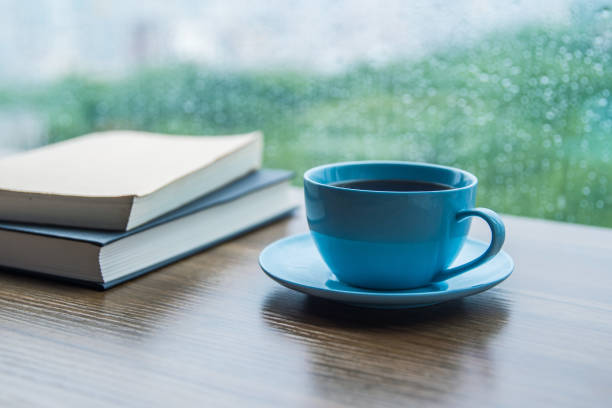 istock Cup of coffee with book on table in rain day 1163902775