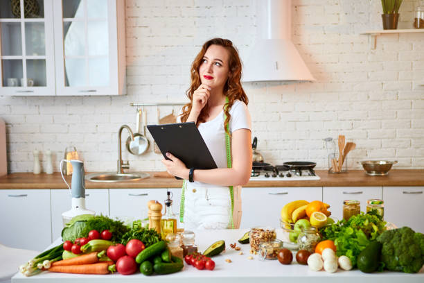 istock Young beautiful woman using tablet while cooking in the modern kitchen. Healthy eating, vitamins, dieting, technology and people concept. Losing Weight 1163902784