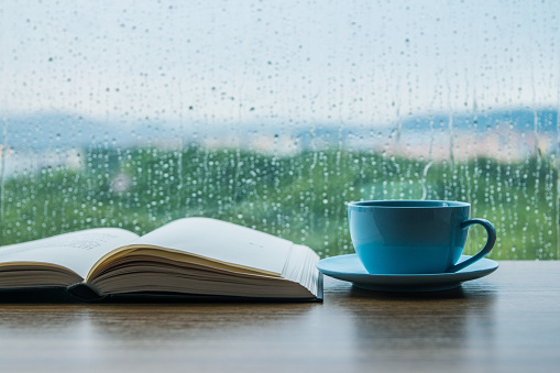 Cup of coffee with book on table in rain day