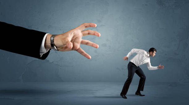 istock Business man running away from a huge hand concept 1163902916