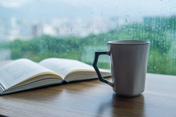 Cup of coffee with book on table in rain day stock photo