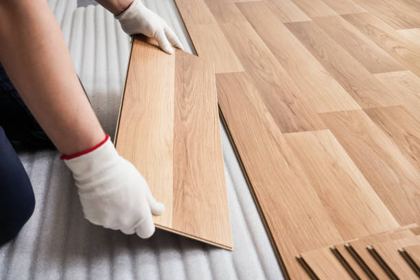 Installing laminated floor, detail on man hands with white gloves fitting wooden tile, over white foam base layer stock photo