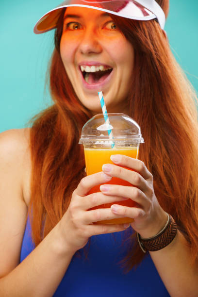 istock Woman wearing a blue swimsuit and hat drinks fruit juice from a cup 1163903337