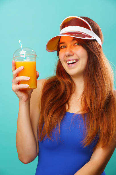 istock Woman wearing a blue swimsuit and hat drinks fruit juice from a cup 1163903579