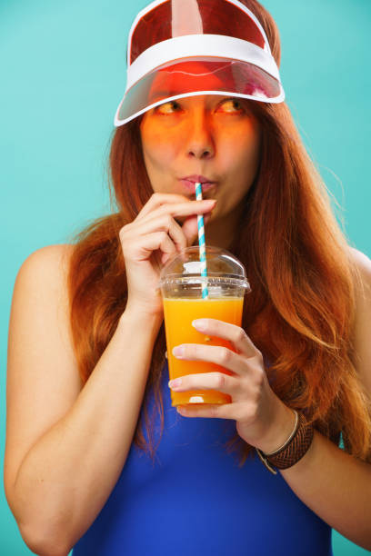 istock Woman wearing a blue swimsuit and hat drinks fruit juice from a cup 1163903618
