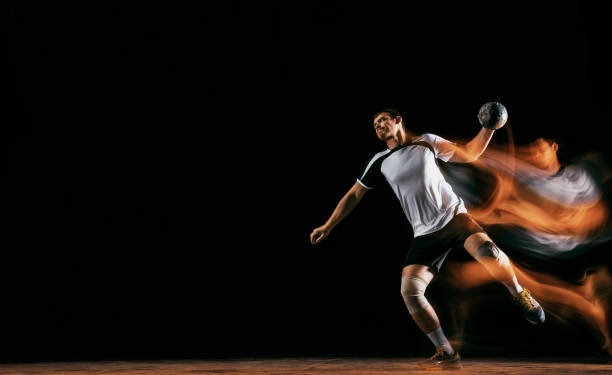 jeune joueur de handball sur le fond foncé de studio dans la lumière mélangée - faute de main photos et images de collection