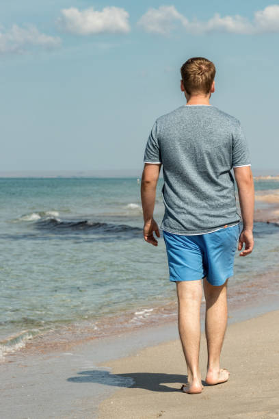 istock Handsome man walking alone on the beach with bare feet. Rest by the beach. 1163905401