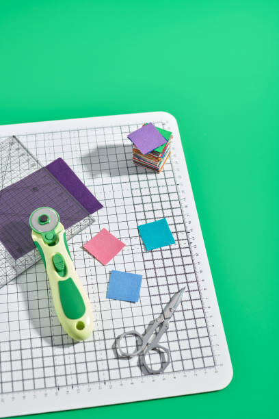 istock Rotary cutter, ruler, bright square pieces of fabric, stack of bright square fabric pieces, scissors on craft mat, green background 1163906408