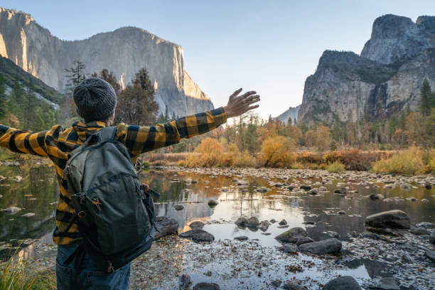 istock Young man arms open at Yosemite valley from the river, reflections on water surface 1163906531