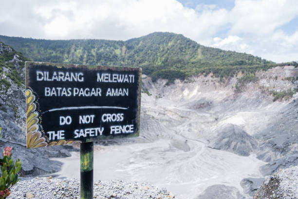 View of the warning sign “Do not cross the safety fence” in English, as same as “Dilarang Melewati Batas Pagar Aman” in Indonesian language at Tangkuban Perahu volcano in Bandung, Indonesia. stock photo