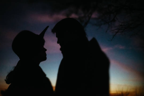 silhouette de couples heureux regardant l'un l'autre et touchant avec la douceur sur le fond du ciel de coucher du soleil et des lumières de ville - shadow focus on shadow women sunset photos et images de collection