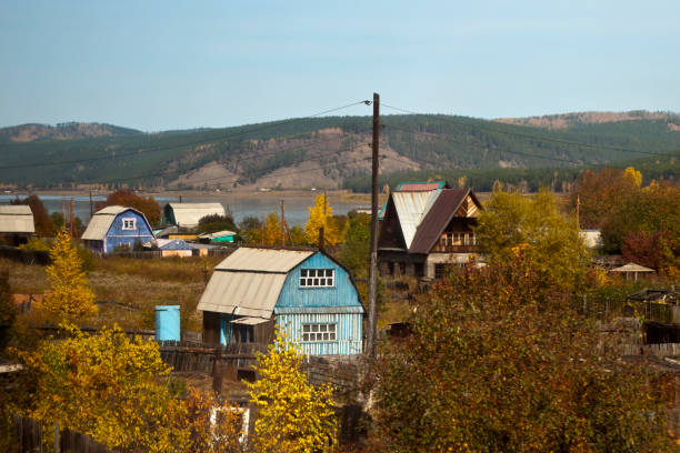 vista autunnale di case dipinte a colori vivaci nel villaggio sul fiume - siberia river nature photograph foto e immagini stock