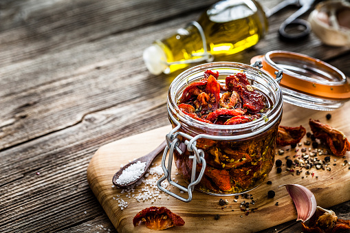 Glass jar filled with fresh organic sun dried tomatoes in olive oil. The composition is at the right of an horizontal frame leaving a useful copy space for text and/or logo at the left. Predominant colors are red and brown. DSRL studio photo taken with Canon EOS 5D Mk II and Canon EF 100mm f/2.8L Macro IS USM.