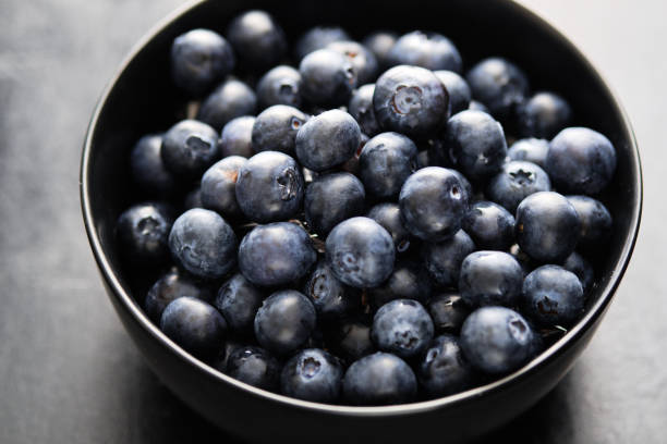 istock Freshly picked blueberries in black bowl on the table. 1163909946