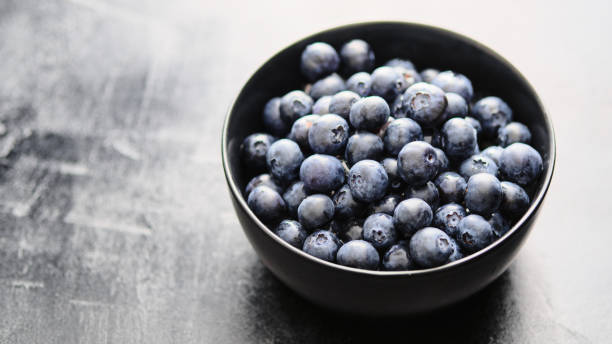 istock Freshly picked blueberries in black bowl on dark background. 1163910015