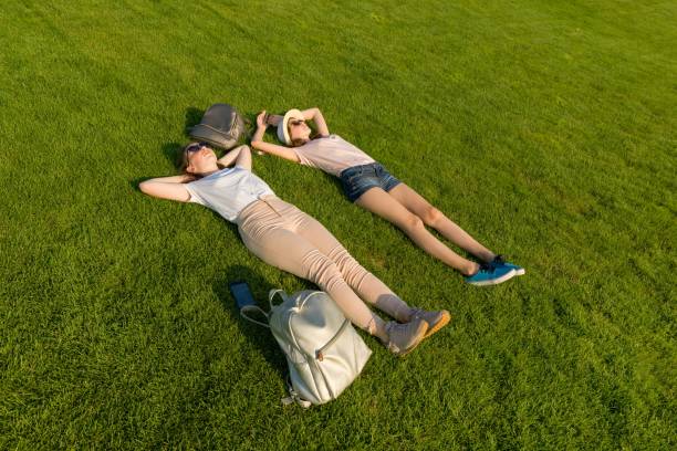 istock Two young female students with backpacks lying on green lawn grass. 1163911886