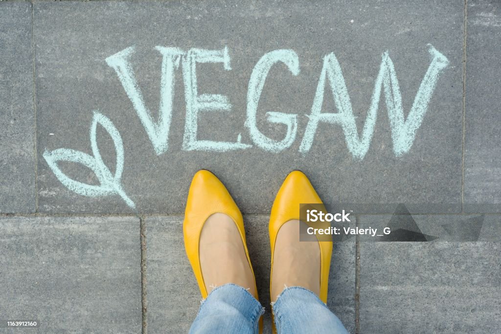 Pies femeninos con texto vegano escrito en la acera gris - Foto de stock de Calzado libre de derechos