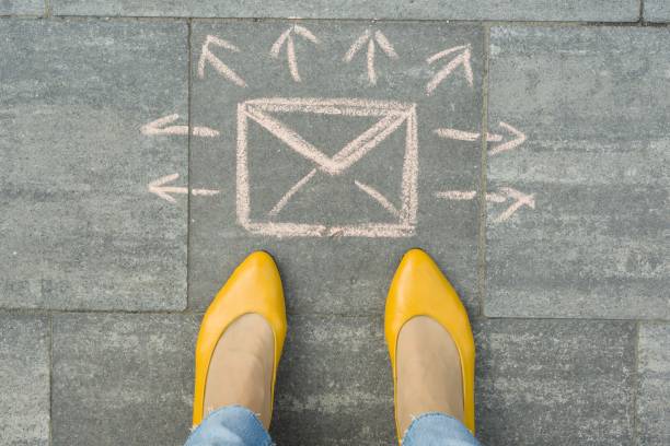 istock Female feet with abstract envelope message letter with arrows in different directions, written on grey sidewalk 1163912338
