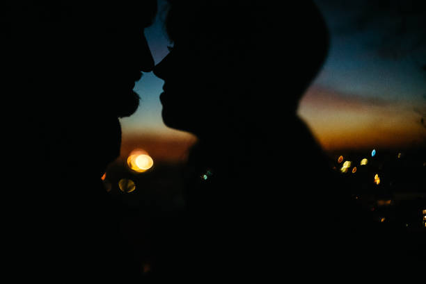 silhouette de couples heureux regardant l'un l'autre et touchant avec la douceur sur le fond du ciel de coucher du soleil et des lumières de ville - shadow focus on shadow women sunset photos et images de collection