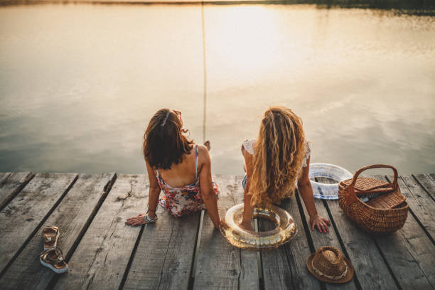 Best friends walking on wooden dock over the lake with inflatable in hands