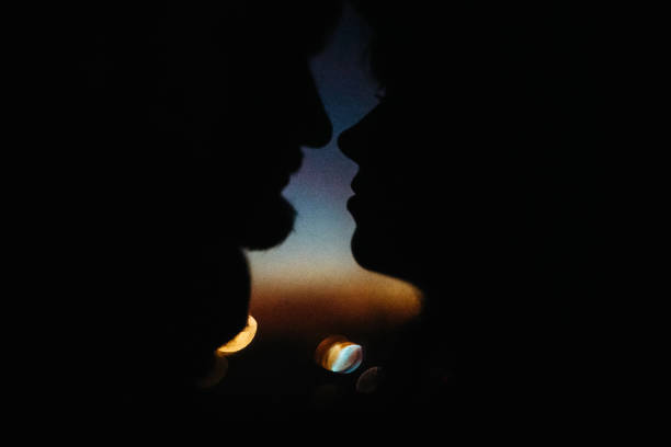 silhouette de couples heureux regardant l'un l'autre et touchant avec la douceur sur le fond du ciel de coucher du soleil et des lumières de ville - shadow focus on shadow women sunset photos et images de collection