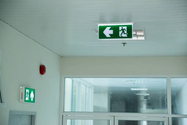istock Sign : Emergency exit sign at path way indoor building public facility that emergency escape route is left. (fire, building, health or safety) require exit signs to be permanently lit 1163921084