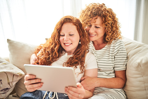 Shot of a happy mother and child using a digital tablet while sitting on a couch together at home