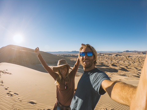 Couple traveling takes selfie picture on sand dunes at sunset
