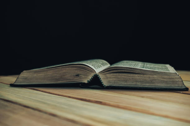 istock Open Bible book on a wooden table and black background. 1163925818