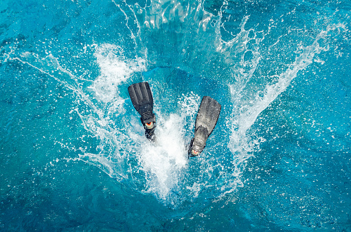 Diver in a wetsuit and flippers jumping in the blue water