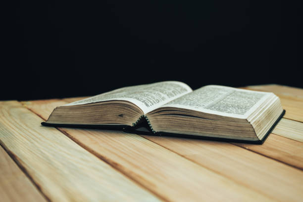 istock Open Bible book on a wooden table and black background. 1163929295