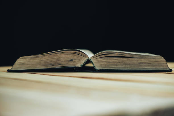 istock Open Bible book on a wooden table and black background. 1163930013