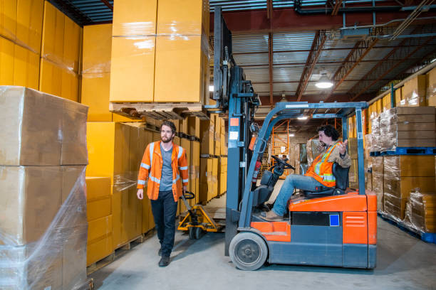 istock An industrial warehouse workplace safety topic.  A worker in the danger zone, walking under a raised forklift carrying a load. 1163932022