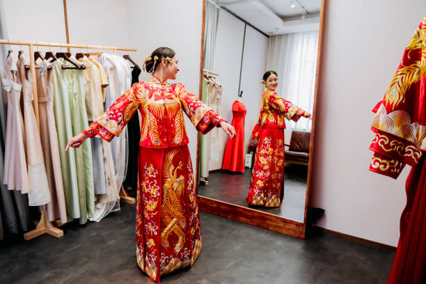 Traditional Chinese bride admiring wedding dress in mirror Young Chinese bride in traditional wedding dress with arms extended admiring her appearance in the mirror. chinese wedding dress stock pictures, royalty-free photos & images