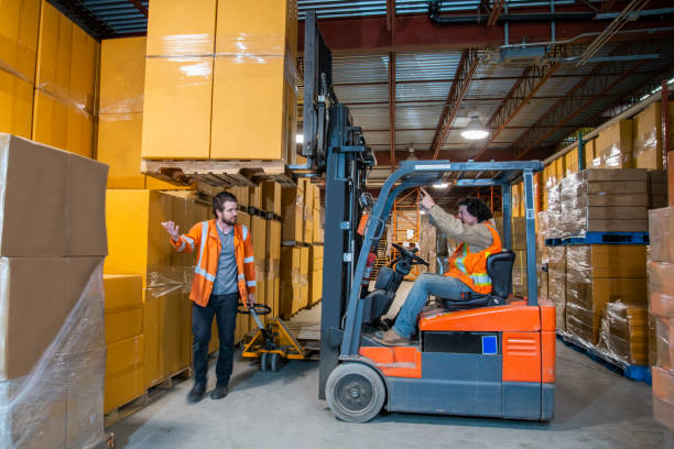 istock An industrial warehouse workplace safety topic.  A worker in the danger zone, walking under a raised forklift carrying a load. 1163934651