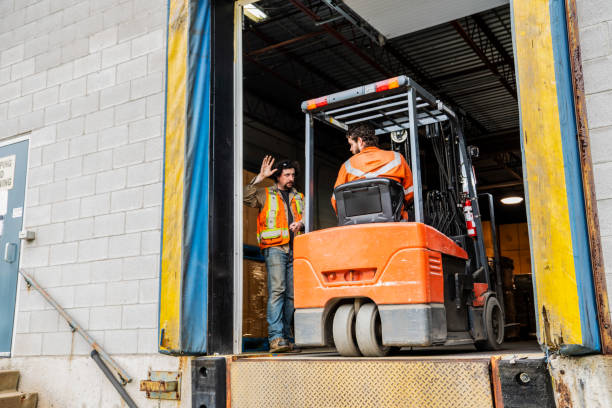 An industrial warehouse workplace safety topic.  A manager or supervisor stops a forklift driver from backing up over a loading dock. An industrial warehouse workplace safety topic.  A manager or supervisor stops a forklift driver from backing up over a loading dock.  Forklift accidents at loading docks are major contributors to serious injuries in the workplace. loading bay stock pictures, royalty-free photos & images