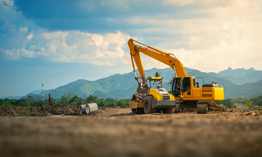 A small tractor works in the sand, filling up a hole. Shovels are on the ground. View from above.