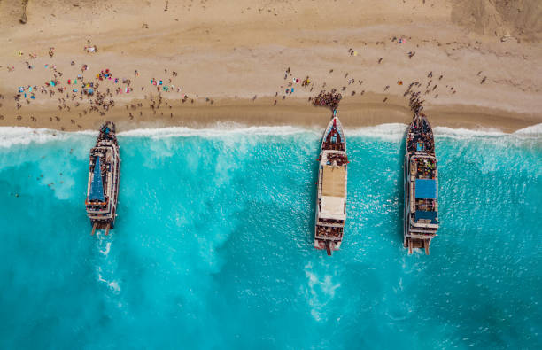 Tourists Arrived At The Beach Aerial view of three tourist boats anchoring on the egremni beach with turquoise colored sea water. egremni beach lefkada island greece stock pictures, royalty-free photos & images