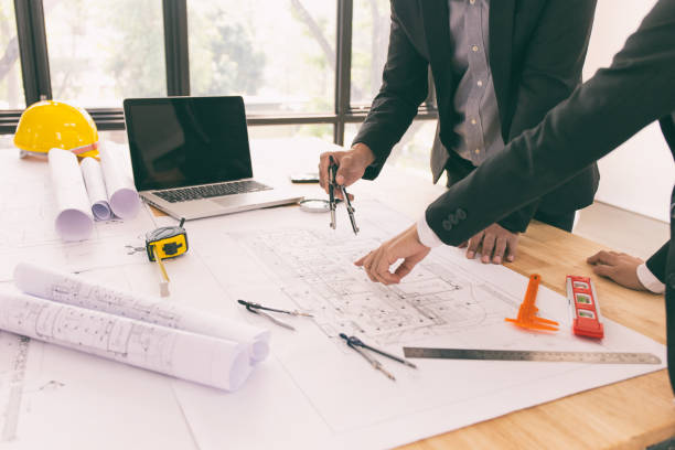 istock Young architect woman drawing building plan at working desk with her team worker. 1163958008