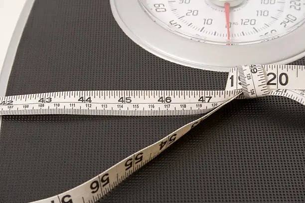 A close up of a weight scale with a measuring tape tied around the middle of the scale