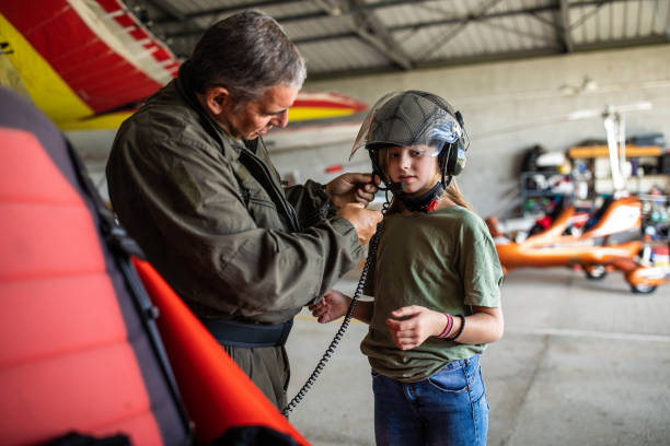 Let me help you with your helmet Mature pilot instructor helping to teenage girl with helmet in the airplane hangar airplane commercial airplane propeller airplane aerospace industry stock pictures, royalty-free photos & images