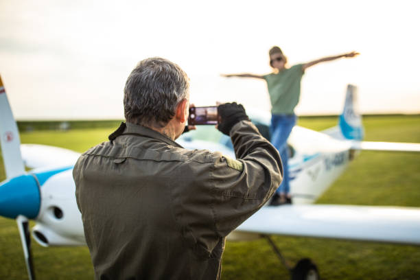 Father pilot photographing his daughter while standing on plane with mobile phone
