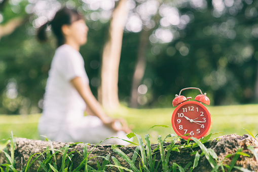 Alarm clock red on the grass. Women of meditation and yoga in the park space behind a blur.